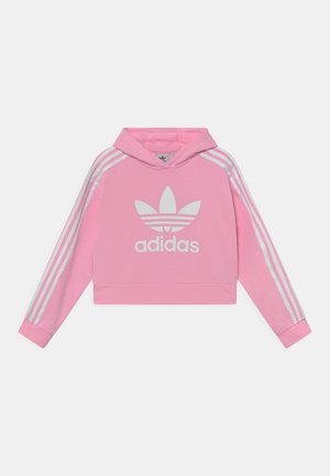 Hoodie rose court avec logo trèfle Adidas et texte sur le devant, trois bandes blanches courant le long de chaque manche.