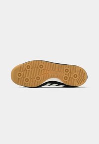 Black and white sneaker with a textured gum sole, featuring three white stripes, round tread patterns, and Adidas branding on the side.