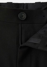 Pantalones negros con una textura suave, que presentan un cierre de botón, cremallera y trabillas para el cinturón; diseñados con un acabado limpio y ajustado.