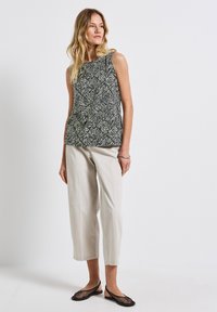 Ärmelloses Oberteil mit schwarz-weißer Blattsilhouette, kombiniert mit hellbeigen, knöchellangen Hosen und schwarzen Mesh-Ballerinas. Einfaches und entspanntes Design.