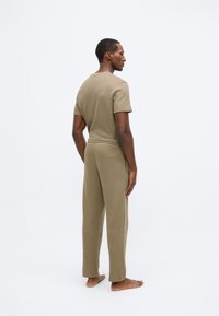 Olívazöld színű, texturált anyagból készült otthoni ruhaszett; rövid ujjú felsőből és rugalmas derékpánttal ellátott, hozzáillő nadrágból áll.