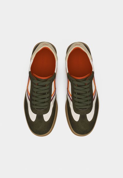 Paire de baskets à lacets vertes, blanches et orange avec semelles en gomme, vues de dessus sur un fond gris clair uni.