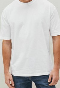 Biała bawełniana koszulka z okrągłym dekoltem i krótkimi rękawami, charakteryzująca się luźnym krojem i brakiem widocznych wzorów lub akcentów.