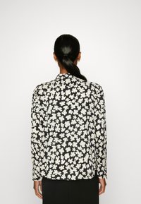 Blusa a maniche lunghe in tessuto nero con motivi floreali bianchi. Sul retro presenta una vestibilità comoda con colletto e polsini abbottonati.