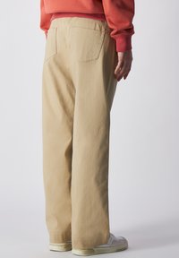 Beige, lässige Baumwollhosen mit glatter Textur. Sie verfügen über zwei Gesäßtaschen und ein gerades Bein-Design, kombiniert mit weißen Sneakers.