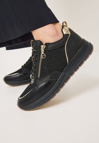 Scarpe sportive nere con tomaia in tessuto testurizzato, dettagli dorati, chiusura con lacci nella parte frontale e zip. Suola in gomma con finitura beige.