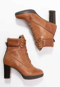 Botines de cuero marrón con cordones en la parte delantera, cuello acolchado, detalles en hardware dorado y tacón grueso y estriado.