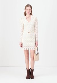Mežģīņu kleita off-white krāsā ar zigzaga rakstu, V veida kakla izgriezumu, garām piedurknēm, ar sasprindzinātu jostasvietu, papildināta ar bežs krāsas rokassomu un brūniem potīšu zābakiem.
