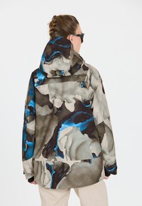Mehrfarbige Jacke mit einem abstrakten Muster aus Braun, Grau und Blau. Sie verfügt über eine Kapuze und einen lässigen Schnitt, mit sichtbaren Nahtdetails.