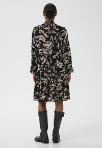 Mustade ja kreemjas toonides mustriga pikkade varrukatega kleit, millel on võtmeauguga seljaosa, mitmekihiline ääre, kantud koos mustade põlvikutega. Sile tekstuur.