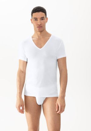 T-shirt bianca con scollo a V in un tessuto texturizzato, maniche corte, abbinata a slip bianchi aderenti, esposta su uno sfondo chiaro.