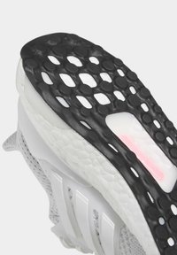 Grå sneakersula med en texturerad svart gummiyta med cirkulära utskärningar och en vit mellansula med en rosa detalj.