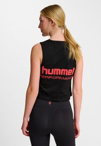 Zwart mouwloos crop top met een opvallend rood "hummel PERFORMANCE" logo op de achterkant. Het materiaal lijkt zacht en lichtgewicht te zijn.