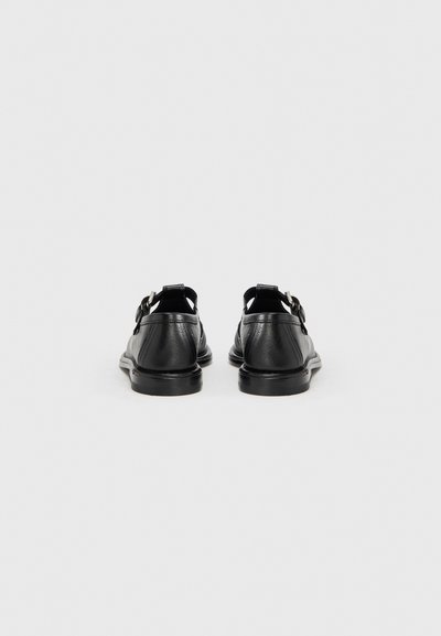 Μαύρα δερμάτινα παπούτσια με λείο υφή, στρογγυλεμένο σχήμα και δύο ασημένια αγκράφα λεπτομέρειες. Διαθέτουν χαμηλή, επίπεδη σόλα από καουτσούκ.