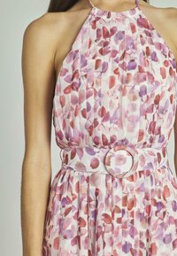 Vestido halter con estampado floral en tonos rosa y púrpura, con pliegues, que cuenta con un cinturón ancho y detalle de hebilla circular. Tejido ligero y texturizado.