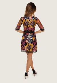 Czarna siatkowa sukienka z kolorową haftowaną florystyką, półdługimi rękawami oraz dopasowanym gorsetem, uzupełniona czarnym paskiem w talii.