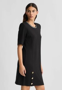 Vestito nero a maniche corte con scollatura rotonda, rifinito in bianco, con silhouette dritta e bottoni dorati lungo la parte frontale.