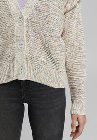 Mehrfarbiger Strickcardigan mit V-Ausschnitt, großen Knöpfen, gerippten Bündchen und strukturiertem Stoff, kombiniert mit schwarzen Jeans.