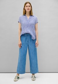 Blå- och vitrandig kortärmad skjorta med krage, kombinerad med löst sittande ljusblå vida jeans och beige sneakers med gröna accenter.