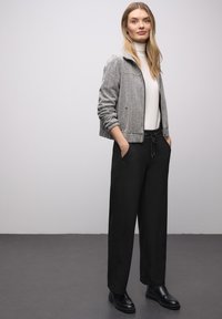 Graue, strukturierte Bomberjacke über einem weißen Rollkragenpullover, kombiniert mit schwarzen, weit geschnittenen Hosen und schwarzen Stiefeletten. Einfaches, modernes Design.