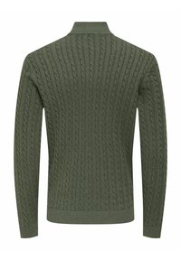 Pull en maille torsadée de couleur vert foncé, avec des côtes verticales, un col haut et des manches longues. Le tissu texturé ajoute un intérêt visuel.