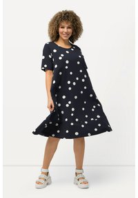 Marineblaues Kleid mit kurzen Ärmeln, versehen mit großen weißen Pünktchen. Hergestellt aus glattem Stoff, hat es eine ausgestellt Silhouette und eine Länge bis unter das Knie.