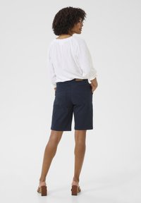 Marinblå shorts med bakfickor, tillverkade av bomullsblandning. I kombination med en vit, löst sittande blus har outfiten en avslappnad design.