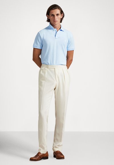 Svetlomodré polo tričko s krátkymi rukávmi, doplnené o krémové nohavice s záhybmi a dvojitým gombíkovým zapínaním; hnedé formálne topánky.