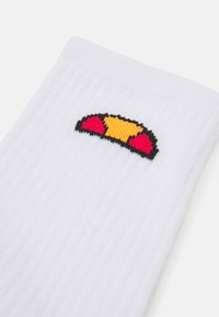 Weiße Socken mit gerippter Textur, die ein farbenfrohes gesticktes Design eines Sandwichs in Rot, Gelb und Schwarz zeigen.