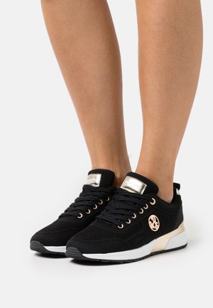 Mustat urheilukengät hengittävästä verkkomateriaalista, joissa kultakoristetut rei'itykset ja logo. Rakenne on kuvioitu, valkoinen keskiosa ja musta ulkopohja.