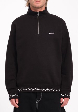 Zwarte zip-up sweatshirt met hoge kraag, voorzien van witte stikselaccenten op de zoom en manchetten, en een klein logo op de borst.