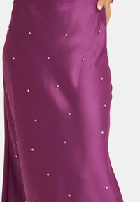 Vestido de satén púrpura con adornos de tachuelas plateadas dispersas, con una textura suave y una silueta ajustada.