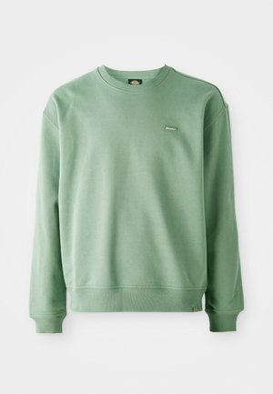 Grøn crewneck sweatshirt lavet af blødt stof, med ribbede manchetter og kant, samt et lille logo tag på fronten. Glat tekstur.