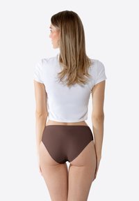 Sous-vêtements marron taille haute avec une texture lisse, associés à un t-shirt court blanc. Modèle vu de dos, cheveux lâchés.