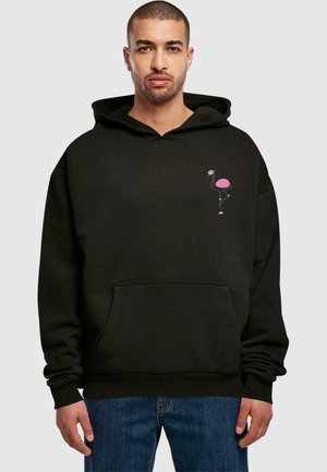 Black oversized hoodie with a front pocket, featuring a pink flamingo graphic on the left chest. Soft fabric with a drawstring hood.