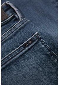 Jeans de denim azul oscuro con un bolsillo cosido y una etiqueta negra con el nombre de la marca "Garcia". La tela tiene una apariencia texturizada.