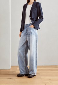 Marinblå blazer med en knapp, i kombination med ljusblå vida jeans. Outfiten har en vit ribbad topp och svarta skor.