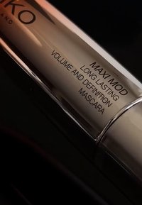 Elegante, metallische Mascara-Tube in Silber. Der Text lautet "MAXI MOD LANGANHALTENDE VOLUMEN UND DEFINITION MASCARA" in Schwarz. Glatte Oberfläche mit minimalistischem Design.