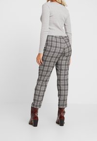 Harmaa pitkähihaaminen paita yhdistettynä musta-valkoisiin ruutukuvioisiin housuihin. Housuissa on slim fit -leikkaus, sileä pinta ja rakenteelliset nilkkasaapaat.