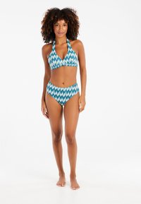 Bikini-setti, joka sisältää halterneck-tyylisen topin ja korkeavyötäröiset alaosat sinivalkoisessa ikat-kuosissa. Sileä pinta ja minimaaliset metalliosat.