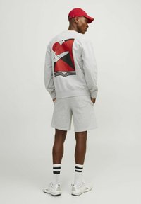 Gray sweatshirt with a bold red and black graphic on the back, paired with gray shorts, white sneakers, and a red cap.