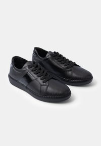 Black leather sneakers with a smooth finish, featuring round toes, textile laces, and stitched detailing along the rubber sole.