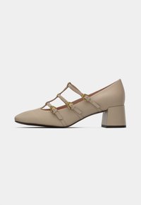 Beige-korkokengät, joissa on kykenevät kärjet, kolmonen säädettävää hihnaa ja kultasävyiset soljet. Silkkinen pinta, minimalistinen muotoilu.