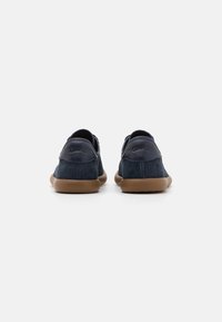 Scarpe casual in suede blu navy con profilo basso, suola in gomma e marchio impresso sul retro, caratterizzate da bordi arrotondati e design minimale.
