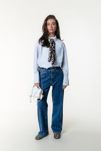 Camisa de botones a rayas en azul claro con mangas oversize, combinada con unos vaqueros de tiro alto en azul con líneas blancas. Accesorio de un bolso blanco.