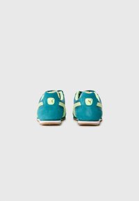 Teal ir limonado žalios Puma sportbačių pora, matoma iš nugaros ant baltos fono, rodančio logotipą ant kulno etikečių.