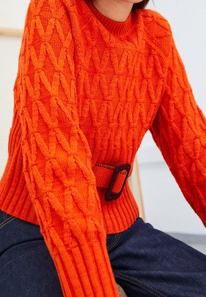 Pull en tricot orange texturé avec un ourlet côtelé et des manches ajustées, présente un détail de ceinture assortie à la taille.