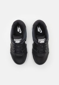 Sneakers atléticos pretos com um cabedal sintético texturizado, detalhes brancos, bico redondo e fecho de atacadores. Apresenta o logotipo "Nike" e a marca "FORCE".