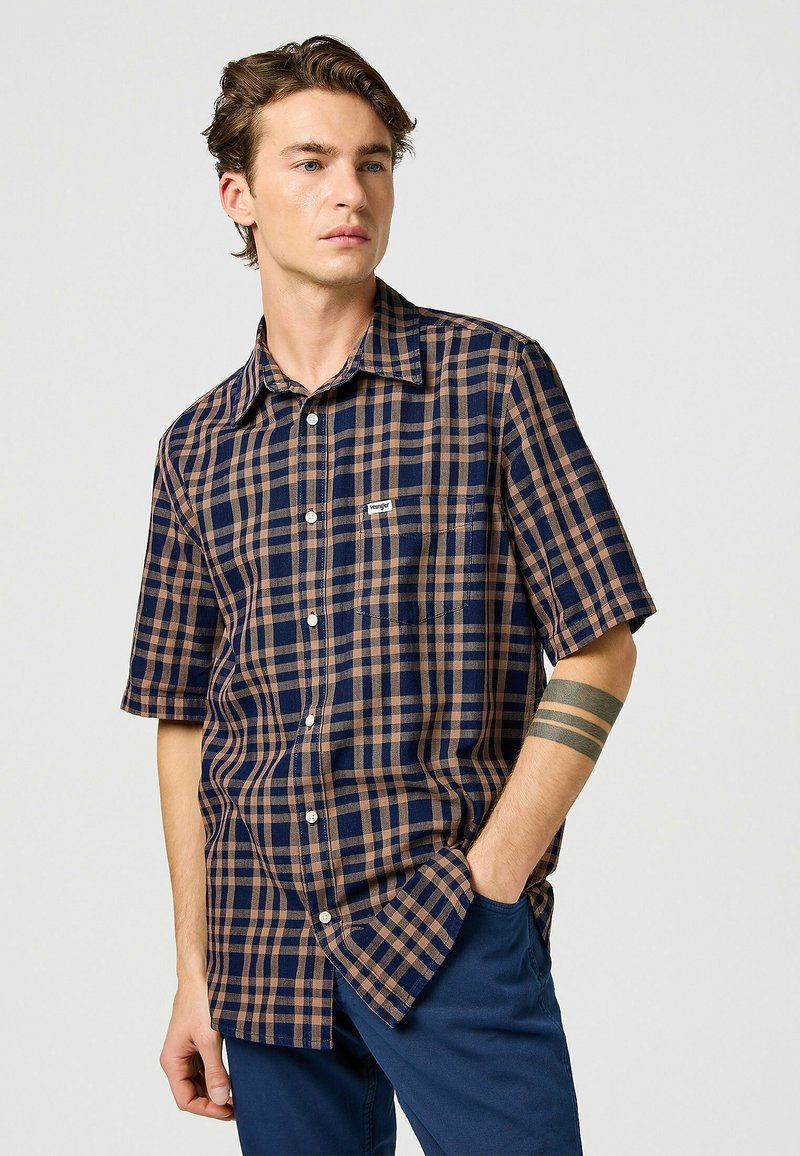 Korte mouwen geruite shirt met een marineblauw en bruin ruitpatroon, lichtgewicht stof, knoopsluiting aan de voorkant en een borstzak. Bevat een merklabel.