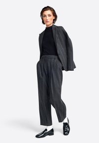 Grau gestreifte Blazer und passende lockere Hose, kombiniert mit einem schwarzen gerippten Rollkragenpullover und schwarzen Slippern. Weiße Socken sind sichtbar.